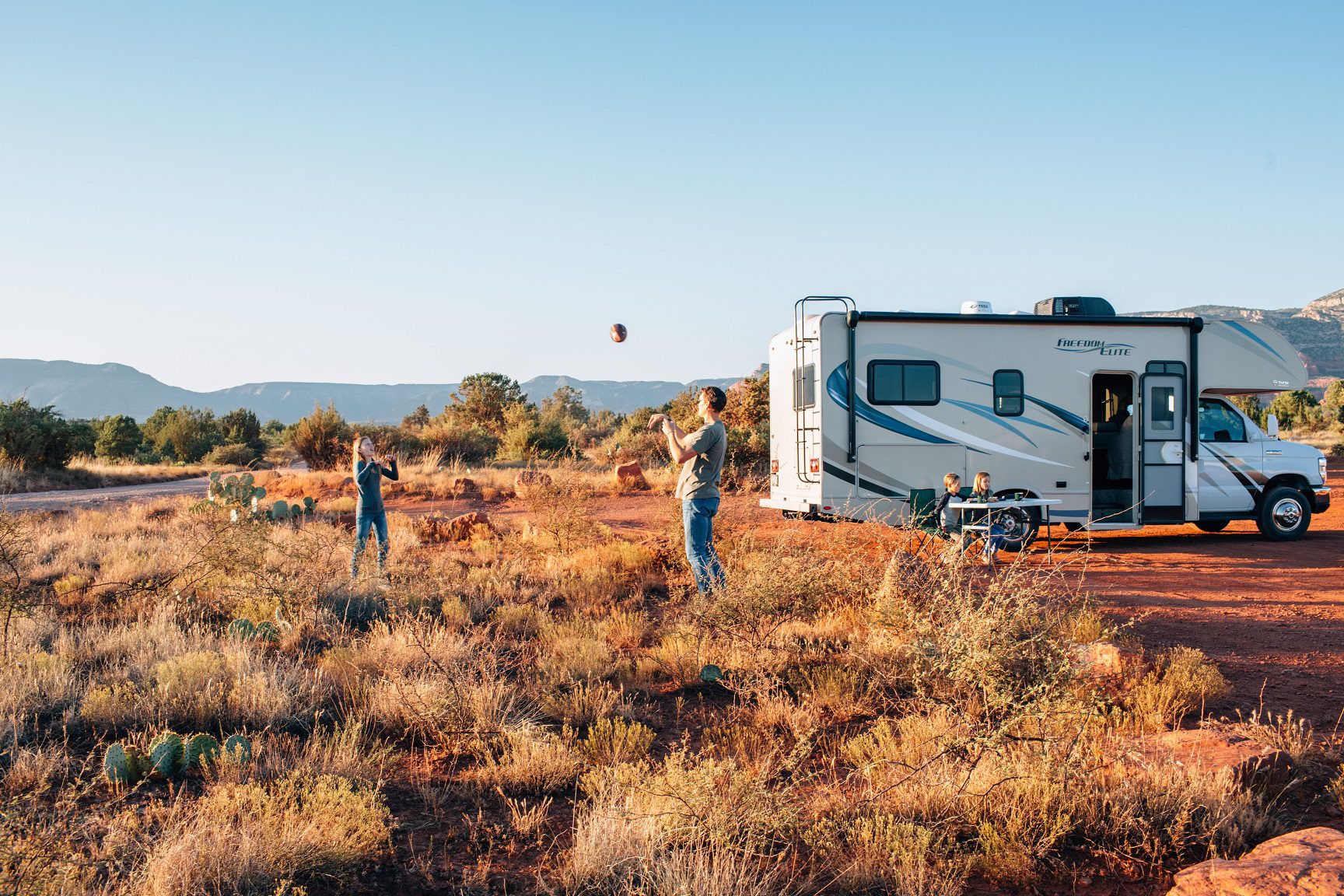 Family playing with a ball in the grass next to their caravan.